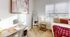 Charming bedroom with plush carpeting, a cozy bed adorned with red accents, a stylish floor mirror, and ample natural light through large windows.