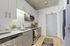 Modern kitchen with sleek white cabinetry, stainless steel appliances, and contemporary lighting. Includes a stylish gray door and elegant wood flooring, perfect for urban living.