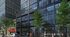 Modern high-rise building with reflective glass facade and lush trees lining the urban street, creating an elegant and inviting atmosphere.