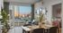 Modern apartment featuring a cozy living area with large windows offering stunning city views, stylish dining setup, and glimpse into a well-lit bedroom.