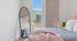 Chic and contemporary bedroom with stylish decor, featuring a full-length mirror, cozy bed with plush pillows, and a large window offering stunning city views.