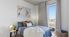 Bright, modern bedroom featuring a cozy bed with plush pillows and a soft blanket, framed art on the wall, and a large window with city views.