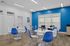 Modern meeting room featuring vibrant blue accent wall, sleek white tables with blue chairs, and ample natural light from large windows.
