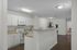 Bright, modern kitchen with white cabinetry and sleek countertops, opening to a spacious living area with stylish lighting and wood flooring.