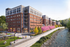 Vibrant riverside apartment complex featuring modern architecture, lush landscaping, and a scenic walkway along a sparkling river.