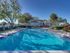 Large apartment community swimming pool with lounge chairs, palm trees, and landscaped courtyard under a clear blue sky.