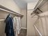 Apartment walk-in closet with hanging rods, shelving, and carpeted flooring for organized storage.