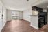 Open apartment living room with wood-style flooring, sliding glass doors, and kitchen with breakfast bar and black appliances.
