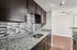 Modern apartment kitchen featuring granite countertops, mosaic tile backsplash, dark cabinetry, and stainless sink.