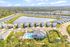 Charming aerial view of a serene residential community featuring quaint houses surrounding a picturesque pond, with a sparkling swimming pool and lush greenery, offering an ideal blend of comfort and tranquility.