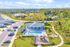 Scenic aerial view of a modern community featuring a sparkling swimming pool, manicured lawns, and lush greenery, all surrounded by serene landscapes and comfortable suburban homes.