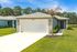 Charming single-story home with a spacious driveway, lush green lawn, and elegant palm tree, set against a serene forest backdrop.
