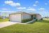 Charming single-story home with a two-car garage, lush green lawn, and serene lakeside views under a bright blue sky.