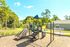 Charming outdoor playground with slides and climbing equipment, set against a lush green backdrop and vibrant skies.