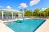 Inviting outdoor pool area with a peacock-shaped float, surrounded by lush greenery and modern lounge chairs beneath a clear blue sky.