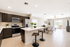 Modern open-plan kitchen and living area with sleek dark cabinetry, spacious breakfast bar with stylish stools, and cozy seating leading to a bright patio overlooking serene water views.