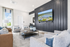 Modern living room with elegant decor, featuring cozy armchairs, a sleek coffee table, and a large wall-mounted TV, enhanced by natural light through large windows.