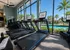 Modern gym facility with treadmills overlooking a serene pool and lush palm trees, promising a refreshing workout experience.