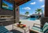 Luxurious outdoor living space with a modern fire pit, inviting seating area, a scenic pool view, and tropical palm trees under a sunny sky.