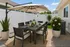 Charming outdoor patio with a modern dining set under a large umbrella, surrounded by lush greenery and blooming flowers.