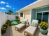 Charming patio oasis with comfortable lounge chairs, vibrant flowers, and a serene yoga area under a bright blue sky.