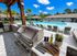 Luxurious outdoor area featuring a modern barbecue grill and elegant poolside with sun loungers, surrounded by lush greenery and blue skies.