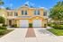 Charming two-story townhouse with sunlit yellow facade, double garage, and lush landscaping, ideal for a vibrant community lifestyle.