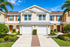 Charming townhouse with two white garage doors, vibrant landscaping, and palm trees under a bright blue sky.