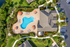 Aerial view of a luxurious apartment complex featuring a vibrant swimming pool with orange umbrellas, beautifully landscaped gardens, and ample parking space.