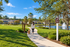 Serene walking trail near vibrant residential community with lush greenery, picturesque lake, and inviting fountain under a clear blue sky.