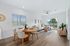 Modern, sunlit living space with elegant dining area, cozy L-shaped sofa, and large glass doors opening to a lush patio.