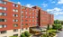 Charming red brick apartment building with lush landscaping and sunny blue skies, offering inviting living spaces.
