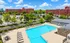 Inviting apartment complex with a large outdoor pool, surrounded by lush green trees, ample lounge chairs, and well-maintained sidewalks under a sunny blue sky.