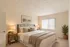 Inviting bedroom with cozy decor, plush bedding, soft lighting, and a serene view through vertical blinds.