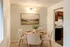 Charming dining space with elegant decor, featuring a round table set for four with soft beige chairs and a serene landscape painting, adjacent to a cozy kitchen.
