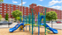 Vibrant apartment community playground featuring colorful slides and climbing structures, offering family-friendly entertainment against a backdrop of lush trees and modern apartments.