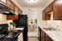 Cozy modern kitchen with rich wooden cabinets, sleek black appliances, and a glimpse into a stylish dining area.