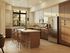Contemporary kitchen at Leawood Village Apartments showcasing stainless steel appliances, wooden cabinets, and a large kitchen island with seating. The space is highlighted by natural light streaming through large windows, creating a warm and inviting atmosphere.