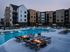 A lavish resort-style pool at The Oslo featuring reef loungers in the water and swim-up bar seating, surrounded by lush landscaping and modern architectural elements, perfect for relaxation and social gatherings.