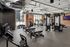 Fitness center with cable machines, adjustable benches, dumbbells and cardio equipment under exposed ductwork