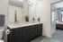 Bathroom with a double vanity, light countertop, dark cabinets and two mirrors, with a doorway to the bedroom