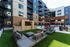 Courtyard lounge with outdoor sectional seating on turf, a stone TV wall, a pergola and string lights overhead