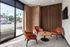 Seating nook with four rust-colored lounge chairs around a round table beside tall street-facing windows