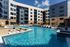 Wide view of the pool with a sunken fire lounge, in-water loungers and umbrellas framed by the apartment buildings