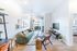 Chic living room with stylish decor, featuring a cozy green sofa, modern TV setup, and bright natural light from large windows.