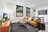 Bright, modern living room featuring a stylish tan sofa, sleek black and white rug, wall art, and abundant natural light from large windows overlooking greenery.