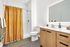Bright modern bathroom featuring sleek wooden cabinetry, a large illuminated mirror, and a vibrant mustard-yellow shower curtain.