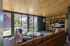 Modern living room with elegant wood ceiling and large glass doors opening to a sunlit patio, featuring a cozy leather sectional and sleek built-in shelving with a flat-screen TV.