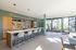 Contemporary communal kitchen and dining area featuring sleek countertops, stylish bar stools, and large windows allowing ample natural light.