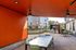 Vibrant outdoor area with modern orange ceiling, sleek dining tables, and a luxurious barbecue setup amidst lush greenery.